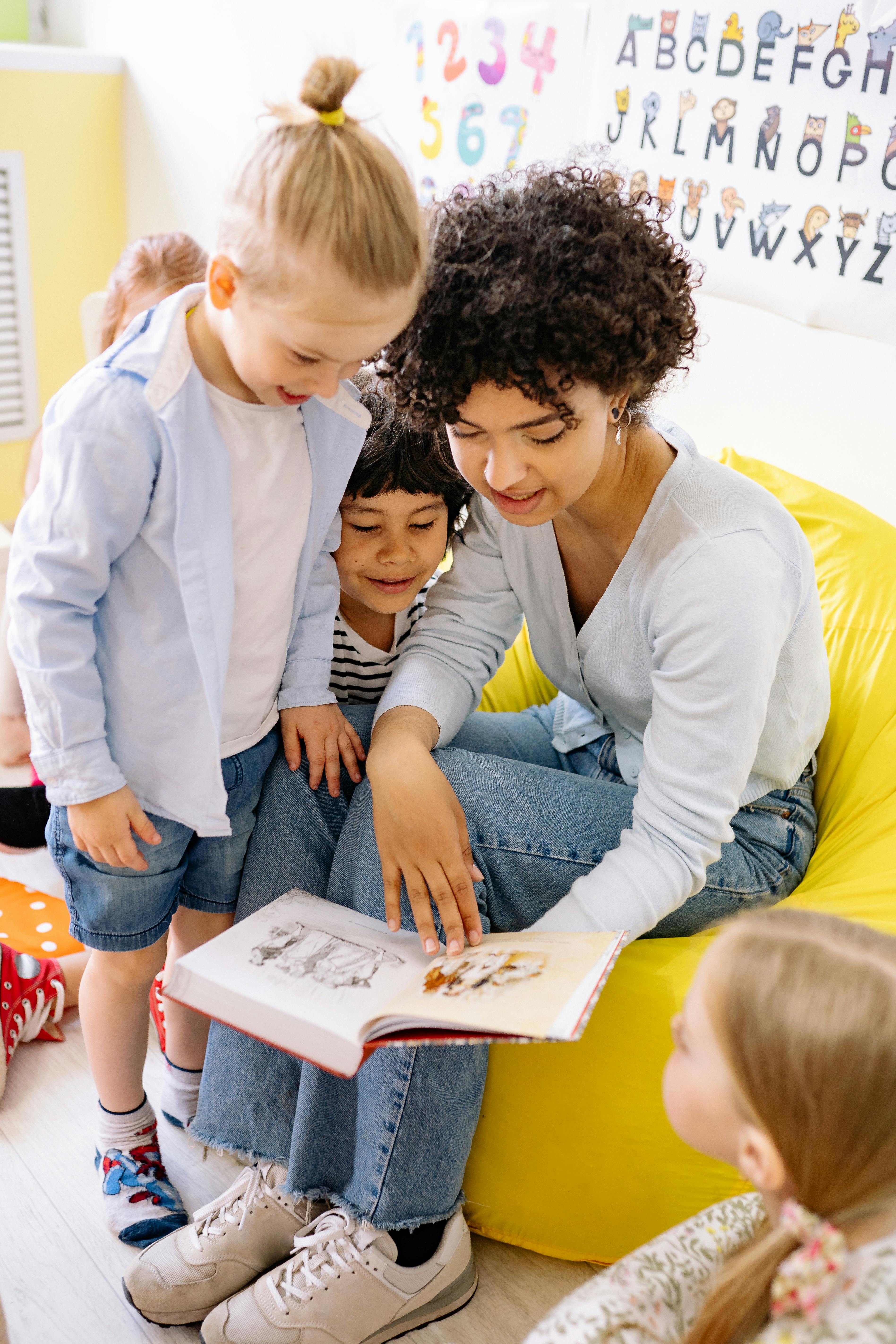 A teacher engaging young children with a storybook in a colorful classroom setting.